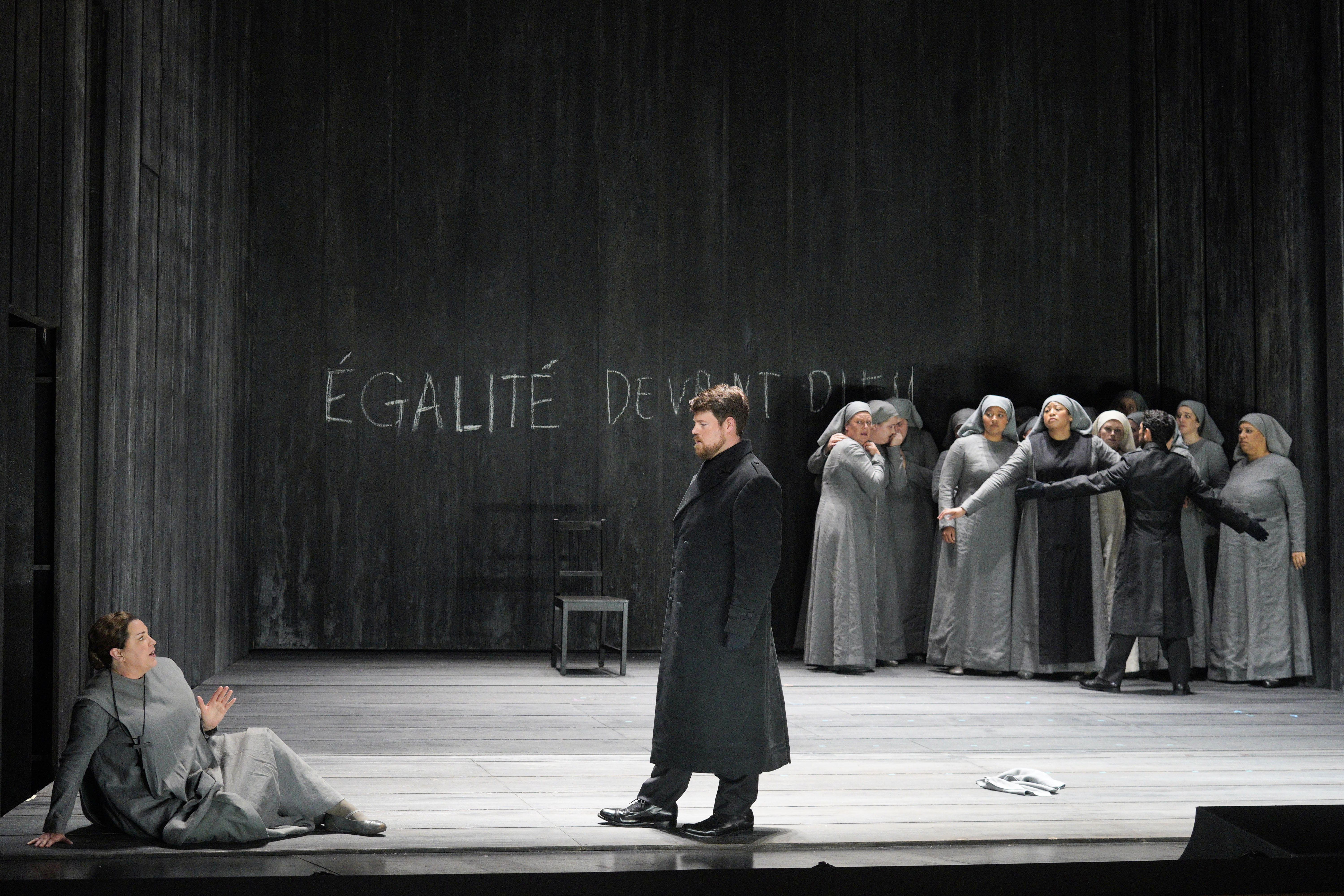 A woman sits onstage as a man stares at her, while another man restrain a group of nuns.